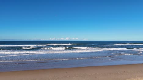 aerial footage of waves gently rolling onto the sandy shore of surfers paradise, gold coast, under clear blue skies