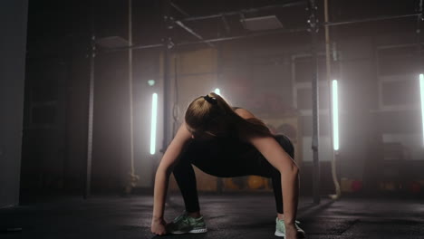 a young slender woman prepares and warms up before training. hitching and stretching muscles after a tedious hard workout in the dark interior of the fitness room