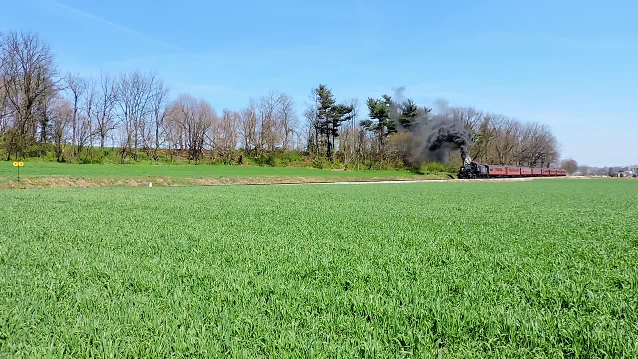 A vintage steam train travels through lush green fields under a clear blue sky emitting black smoke atmospheric lighting cinematic quality rich detail
