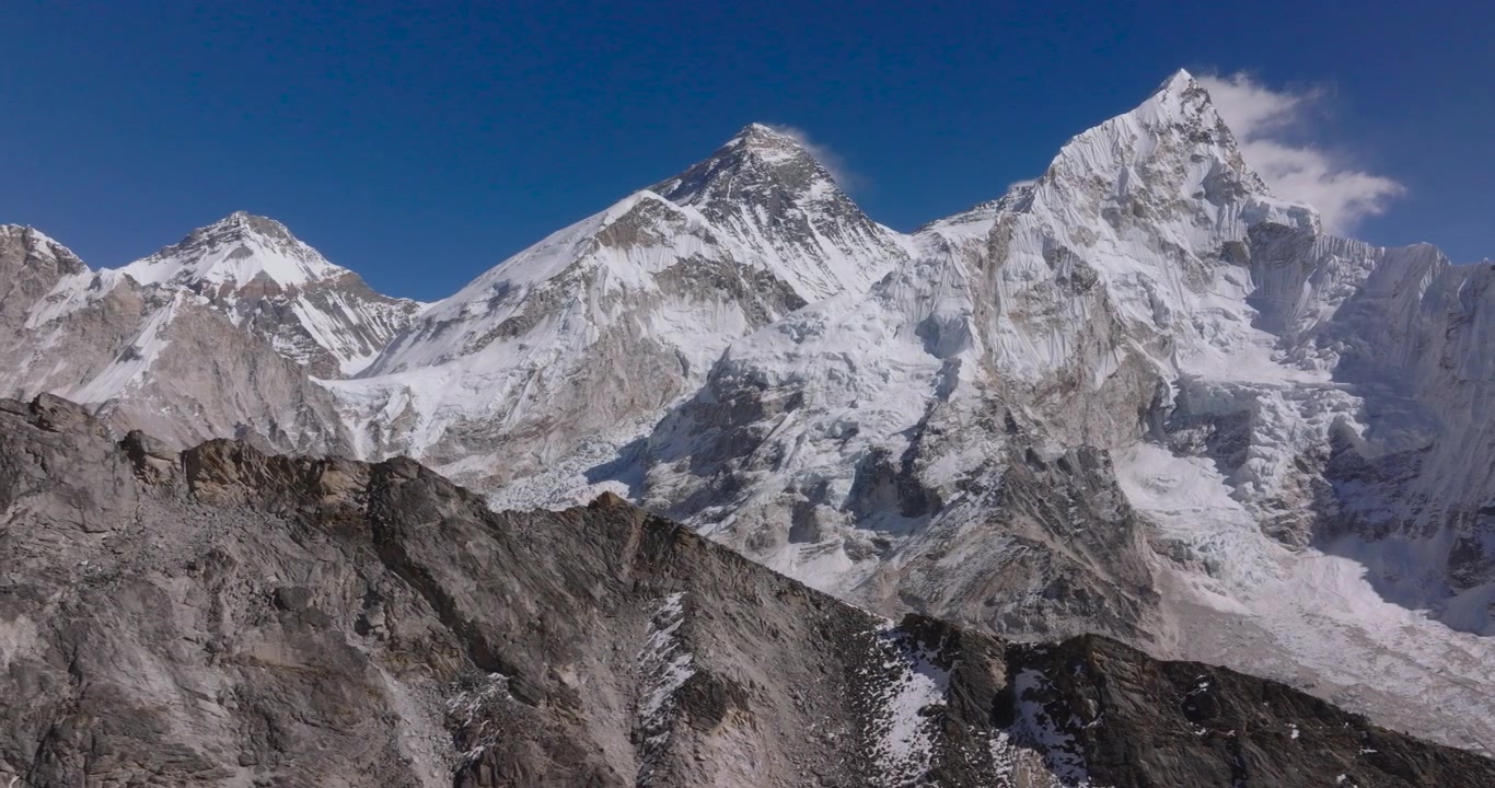 Kala Patthar Everest BaseCamp Nepal, drone-svæveoptagelse af tårnhøje sneklædte Himalaya-giganter med Mount Everest og Nuptse, der rejser sig over mørke klippefyldte højdedrag under en klar blå himmel