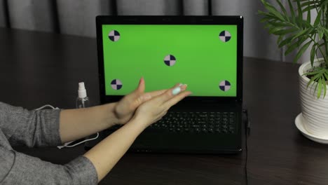 las manos de la mujer usan desinfectante cerca de la computadora portátil con pantalla verde. coronavirus