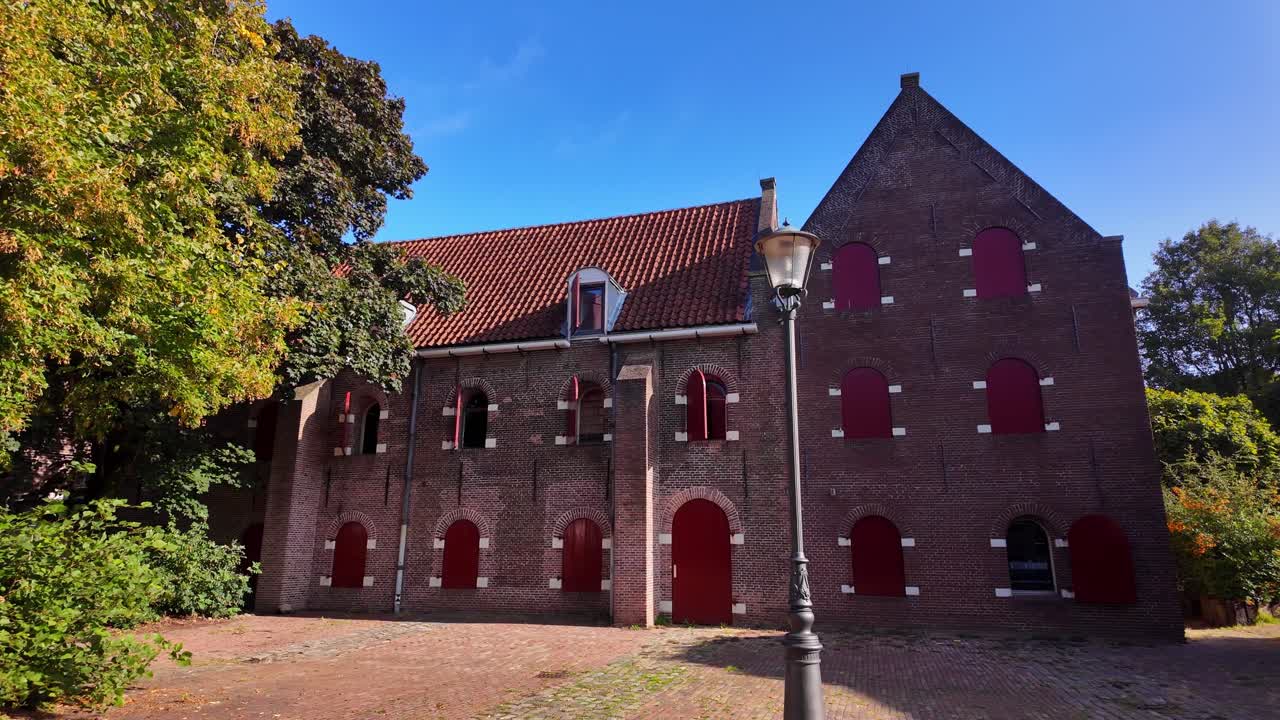 Historic brick building with red shutters and a gabled roof stands near green trees in Coevorden. Location: Coevorden, Drenthe, Netherlands – Coevorden, Drenthe, Nederland