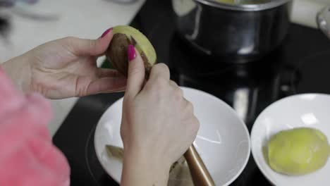 las manos de la ama de casa pelando patatas en la cocina.