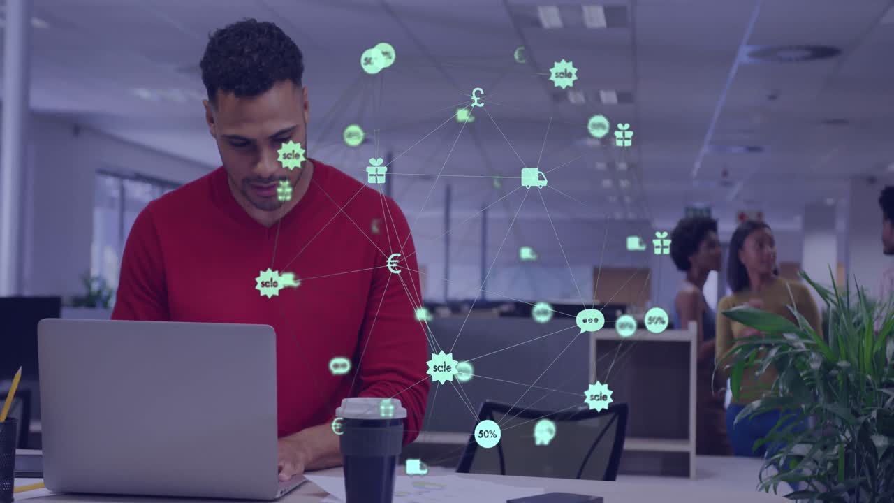 Animation of globe of digital icons over biracial man reading documents using laptop at office