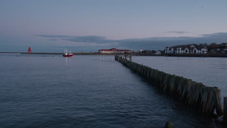 a local red and white fishing boat is returning from the north sea into the river tyne with a flock seagulls following it through the breakwater