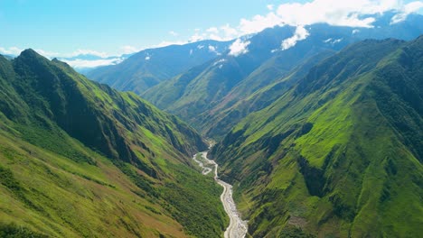 drone establishing overview of deep green mountain valley with winding river and lush andean terrain