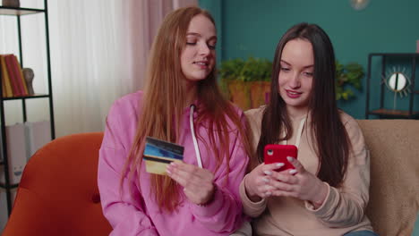 Cheerful-girls-friends-using-credit-bank-card-and-smartphone-while-transferring-money,-purchases