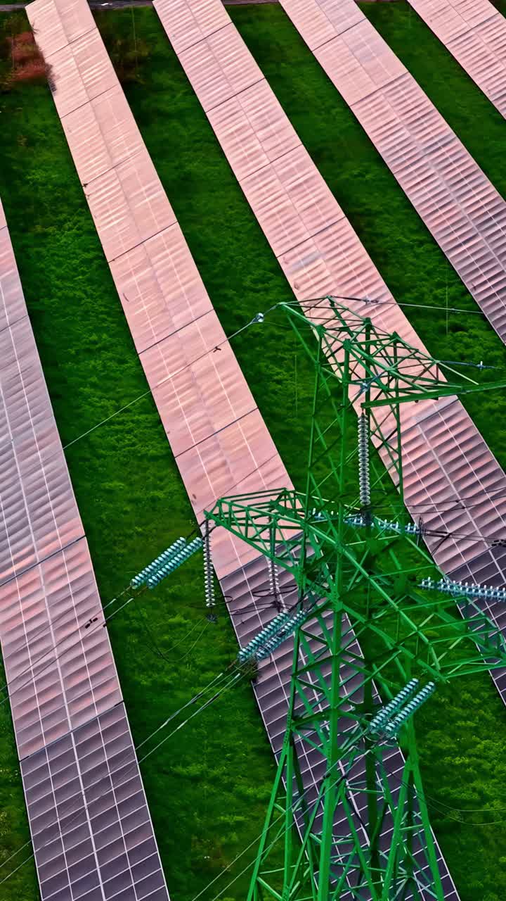 Aerial view of a field of solar panels, with a high-voltage pylon in the foreground