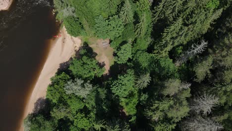 Two-people-walking-away-from-a-kayak-on-the-little-sandy-beach-in-a-forest-on-Gauja-river-in-the-national-park