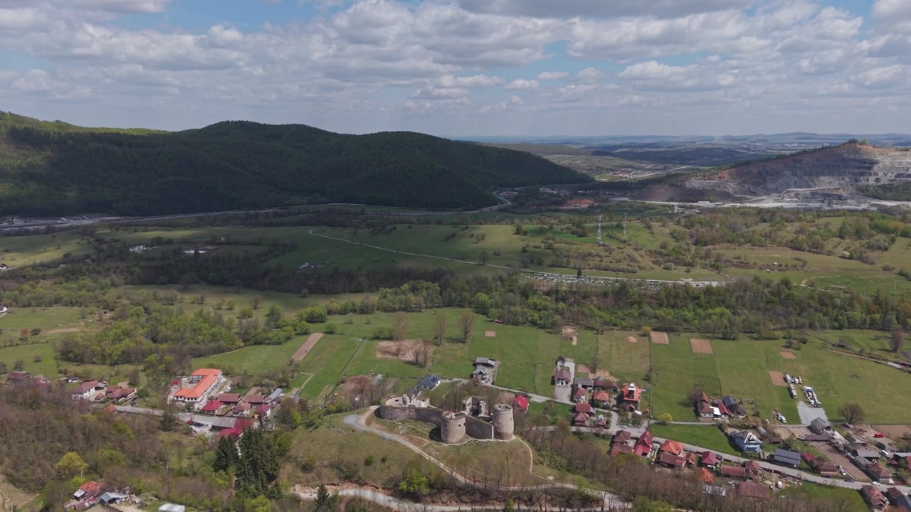 Una vista aerea mozzafiato di un villaggio rurale circondato da valli verdi, dolci colline e montagne boscose sotto un cielo nuvoloso drammatico