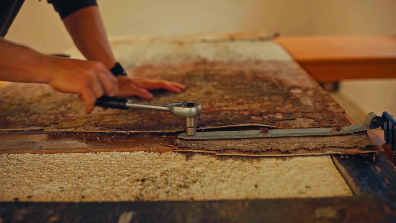 Primo piano di una persona che usa una chiave inglese per rimuovere un pannello metallico arrugginito all'interno.