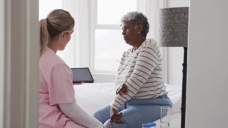 caucasian female nurse and senior african american woman using tablet, copy space, slow motion