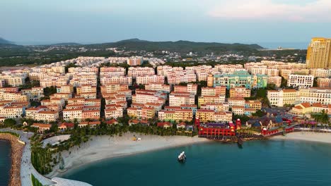 aerial view of the sunset over phu quoc island, vietnam, highlighting a replica italian-style town by the beach. the colorful buildings along the coastline contrast with the serene waters and hills.