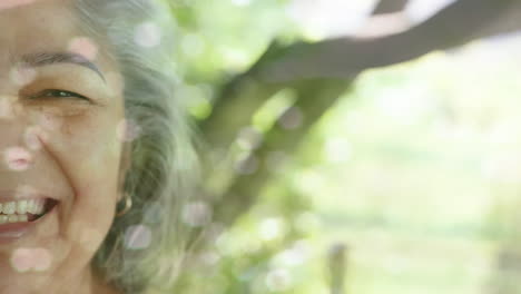 animación de puntos de luz y árboles sobre una mujer biracial mayor sonriente en el jardín