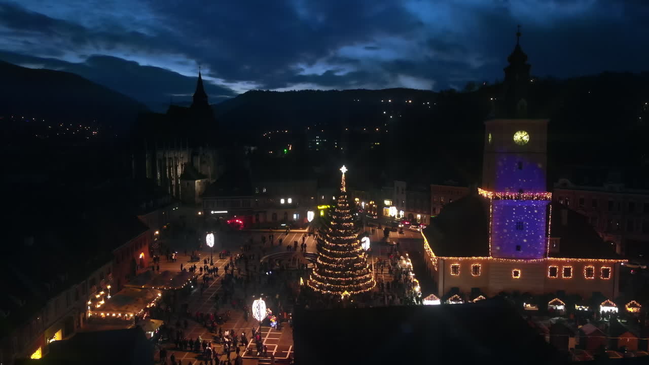 Aerial drone view of The Council Square in Brasov at night, Romania. Old city centre decorated for Christmas. County Museum of History, buildings, people
