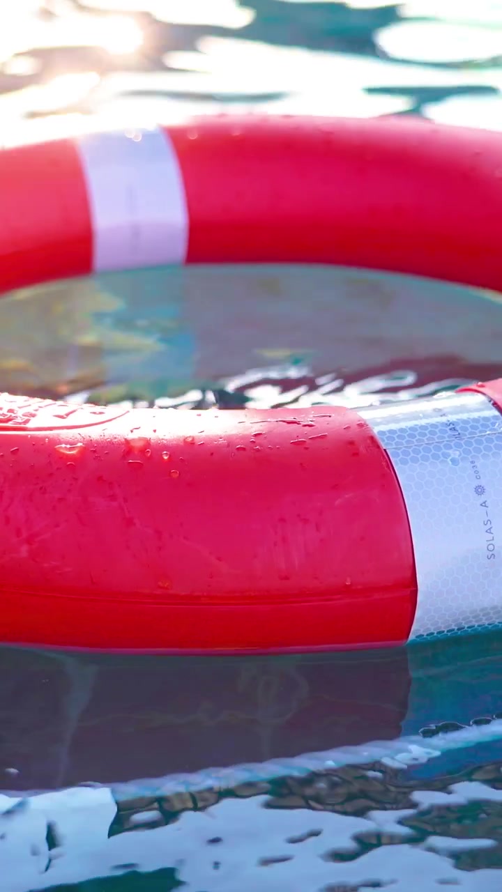 Rippling water surrounds a bright red lifebuoy resting on the surface, reflecting sunlight and bringing a sense of peace. The tranquil pool area invites relaxation and safety.