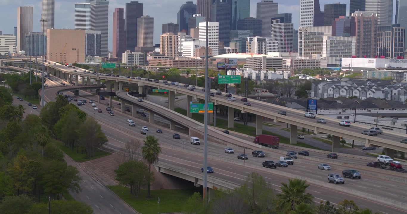 This drone view captures the I 45 South freeway with cars flowing toward the downtown Houston, Texas skyline in the background.