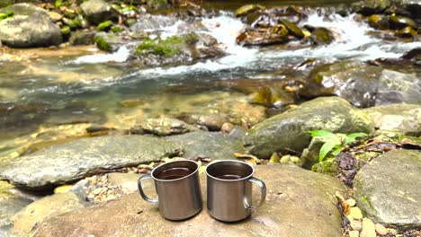 b-roll footage of two coffee mugs full of fresh coffee placed next to a running riverbed in nature