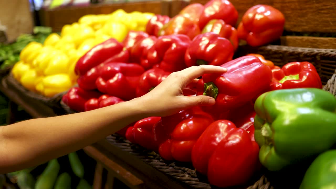 A shopper's hand examines vibrant bell peppers under bright lighting in a Gold Coast supermarket, highlighting fresh produce selection