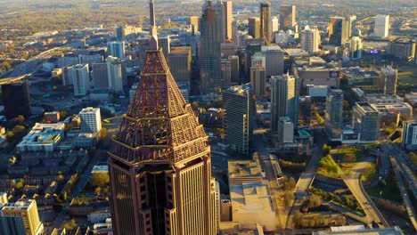 aerial drone shot spiraling around the top of the bank of america building overlooking skyscrapers, traffic, and highways in downtown atlanta, georgia during sunset