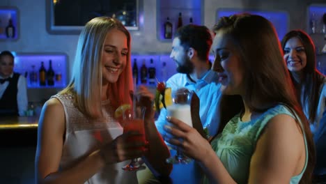 two women toasting their cocktail glasses while partying with friends