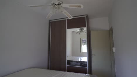 smooth slider clip showcases bright white airbnb apartment bedroom featuring a large wooden closet with mirror, ceiling fan, and minimalist charm. ideal for market listings.
