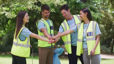 Grupo-Diverso-De-Amigos-Con-Sacos-De-Basura-Azules-En-El-Bosque-Y-Haciendo-Una-Pila-De-Mano-De-Celebración