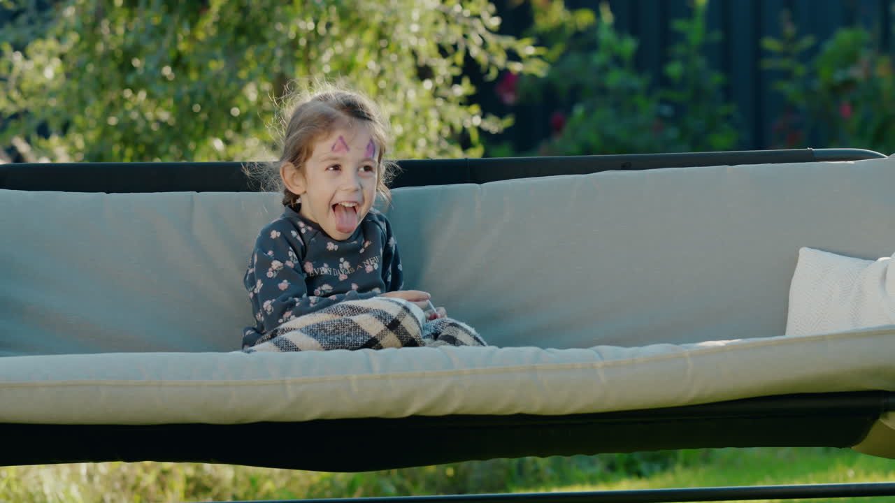 Portrait of a cute girl with face painting on her face, resting in the backyard of a house in a garden swing