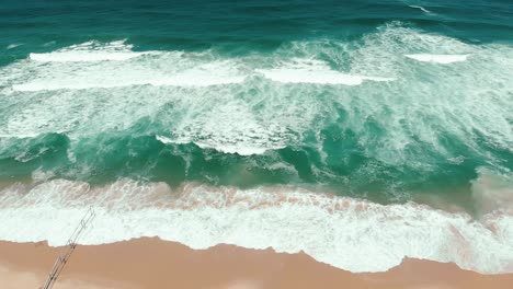 aerial-drone-showing-the-endless-wild-sea-waves-breaking-on-the-sandy-coast-in-slow-motion