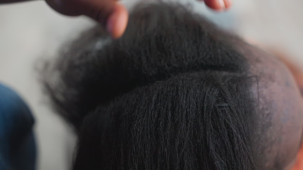 Primo piano di un pettine che seziona capelli naturali, stilista esperto che prepara capelli testurizzati per una treccia con una riga precisa e tensione controllata, pettine a coda e clip usati per file ordinate, mani concentrate.