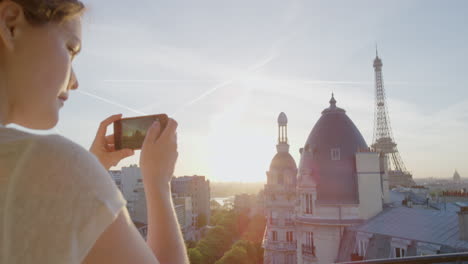 happy woman using smartphone taking photo enjoying sharing summer vacation experience in paris photographing beautiful sunset view of eiffel tower on balcony close up