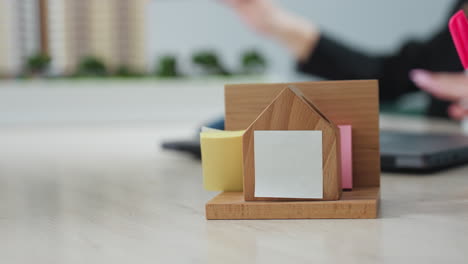 close up of wooden desk organizer holding sticky notes on office table, while blurred professional in background gestures with pencil during project explanation