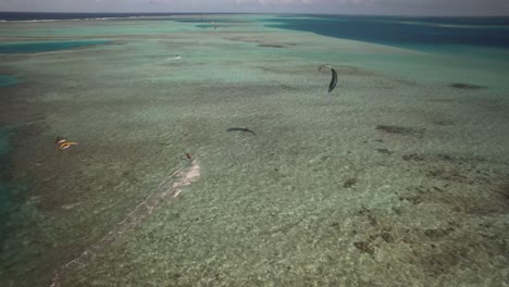 Kite-surfers-gliding-over-clear-turquoise-waters-of-a-coral-reef,-aerial-view