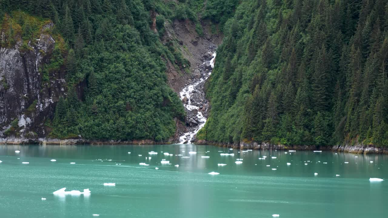 Waterfall's pristine glacial meltwater plunges into the emerald waters of Endicott Arm fjord, Alaska.