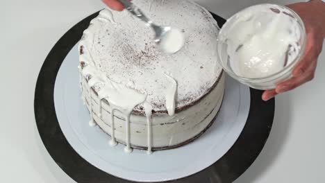 top view of a baker pouring melted white chocolate on the edges of the cake so it drips down the sides.