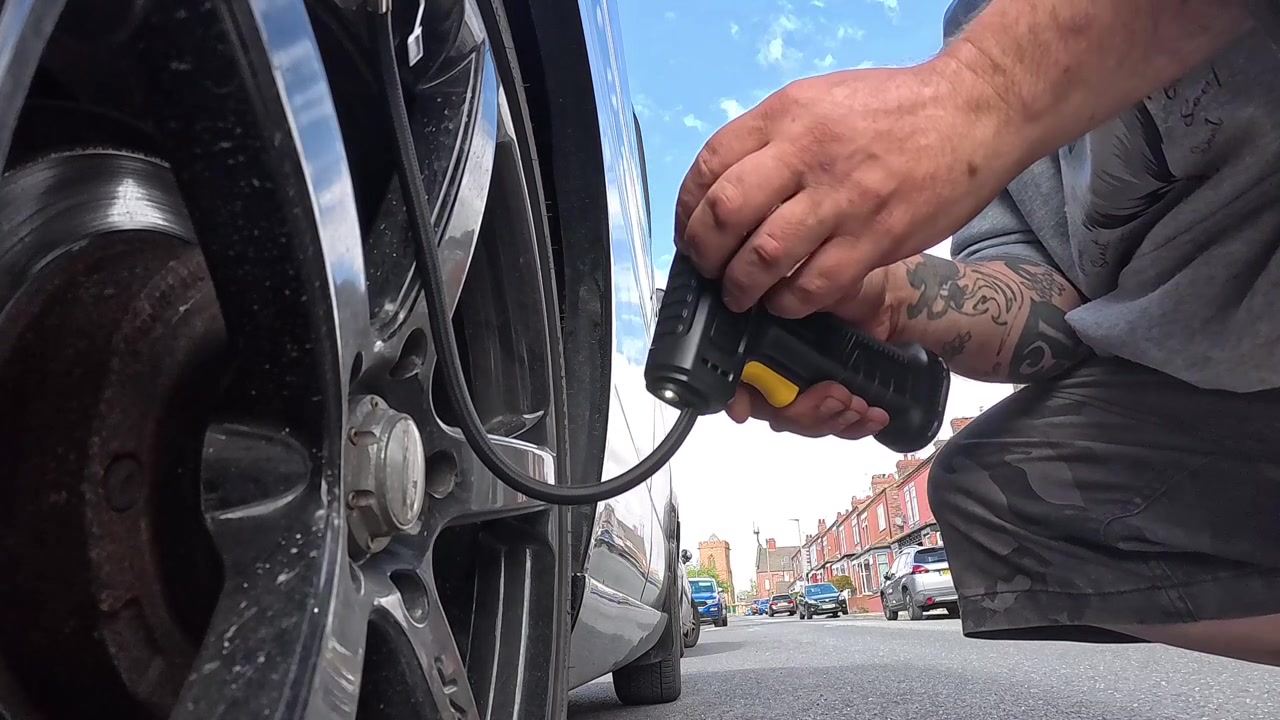 Man holding cordless portable air compressor to inflate van tyre and checking the pressure