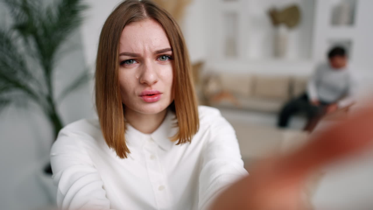 Worried confused concerned young woman looks and points at camera. Close up. Blurred backdrop.