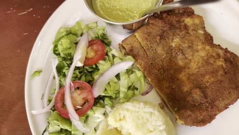 plate showcasing grilled meat with a side of fresh salad, rice, and a small bowl of green sauce. the dish is elegantly presented, highlighting a balanced and appetizing meal, top down shot