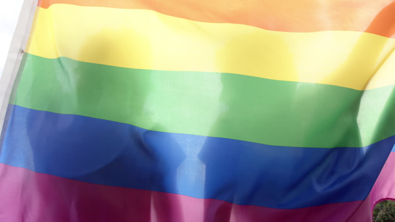 una pareja de hombres homosexuales con una bandera lgbt con arco iris, en cámara lenta
