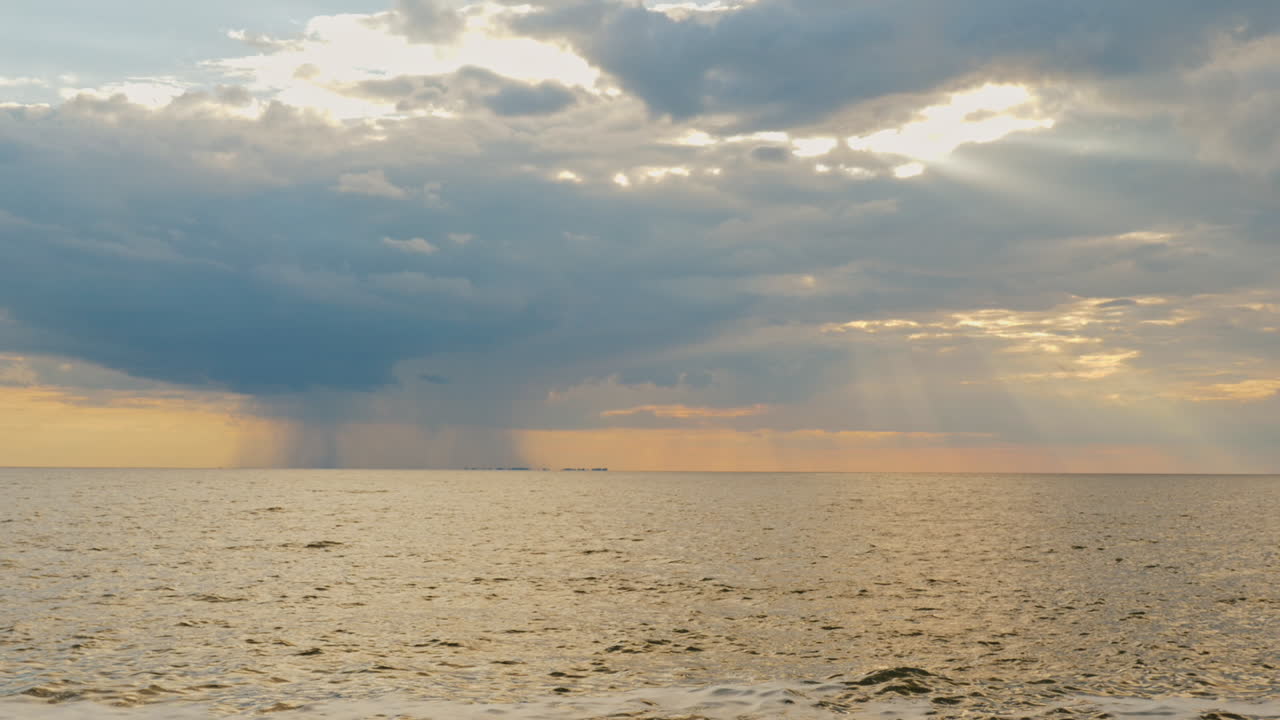 바다로 멀리 떨어진 강한 비와 아름다운 광선으로 지는 태양
