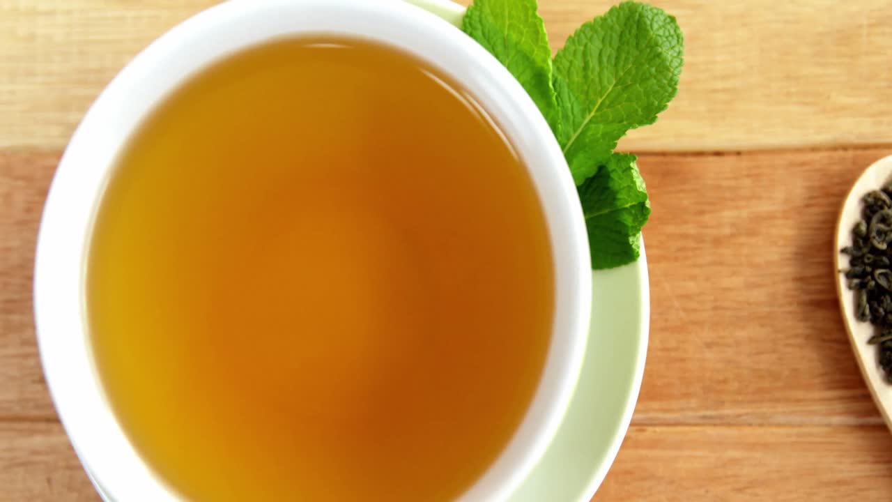 Close-up of tea cup, mint leaves, wooden spoon, dry tea leaves