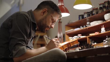 focused luthier varnishing violin in workshop