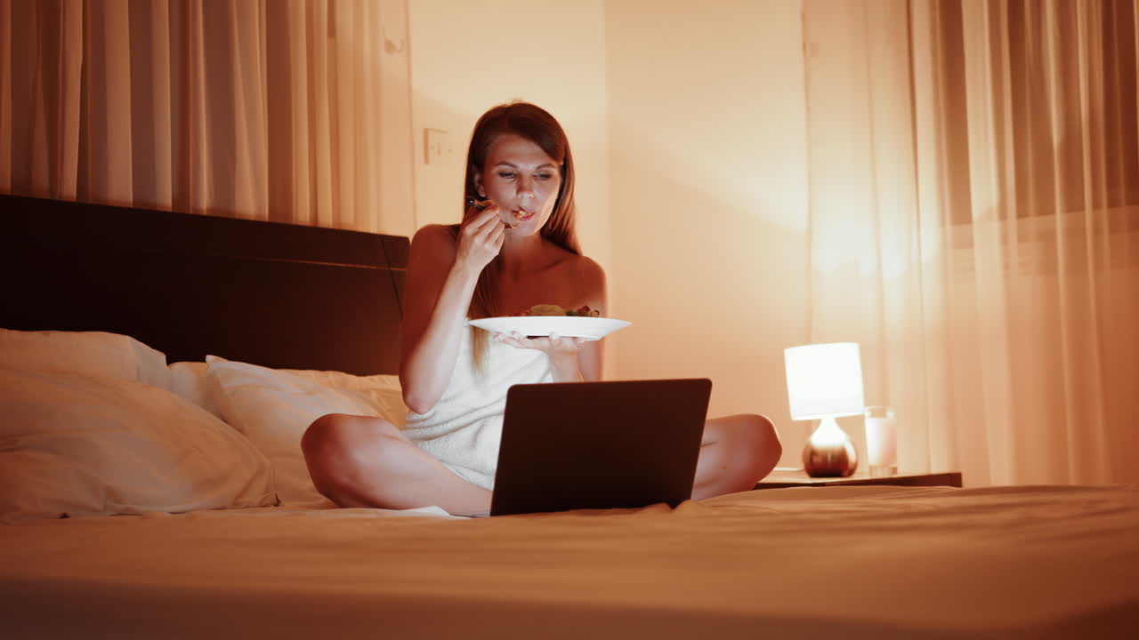 밤에 노트북에서 일하는 동안 침대에서 러드를 먹는 여자