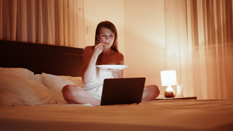 mujer comiendo ensalada en la cama mientras trabaja en la computadora portátil por la noche