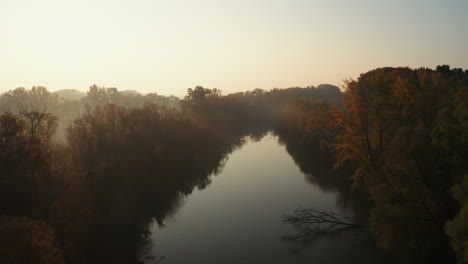 4k aerial shot of morning sunrise with light rays breaking through fog over river and autumn forest