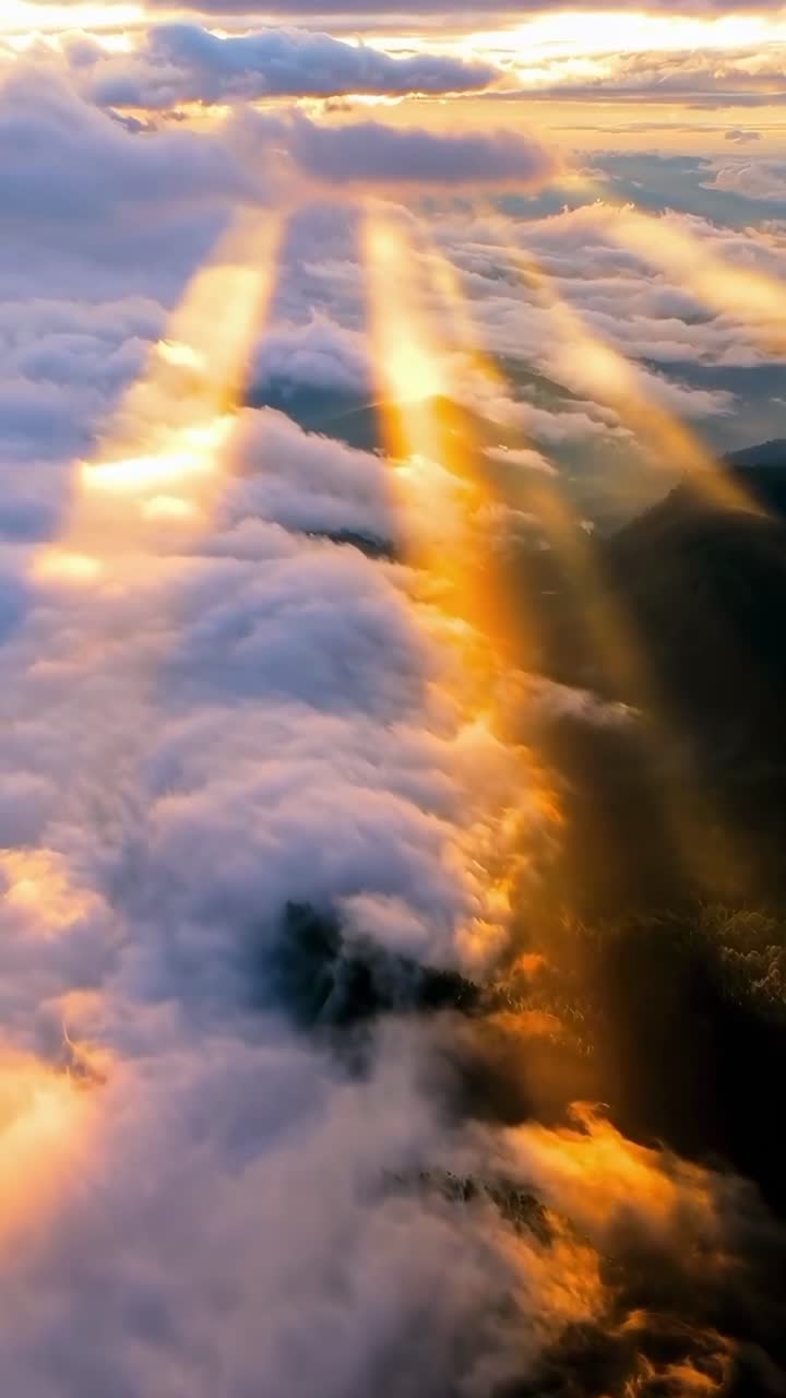 Vista aerea di raggi solari che trafiggono le nuvole sopra le montagne, creando una scena serena simile a un video.