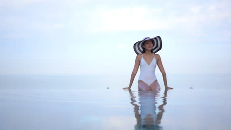 Dream-Like-Scenery-Exotic-Asian-Woman-on-the-Edge-of-Infinity-Swimming-Pool-With-Bright-Endless-Horizon-in-Background,-slow-motion