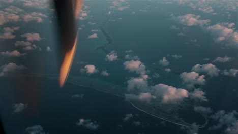 propellor of a small aircraft rotating high above the clouds and an atoll in the south pacific islands of polynesia