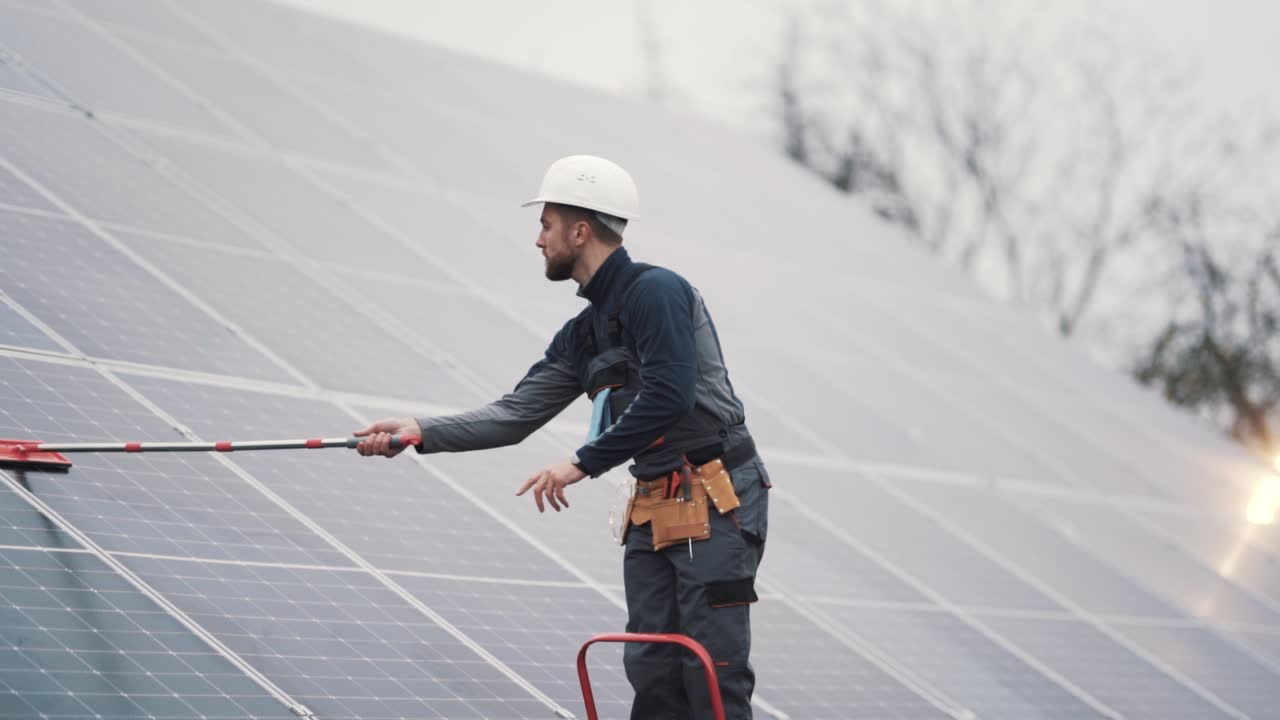 toma general de un joven con uniforme de trabajo limpiando paneles solares con un trapeador