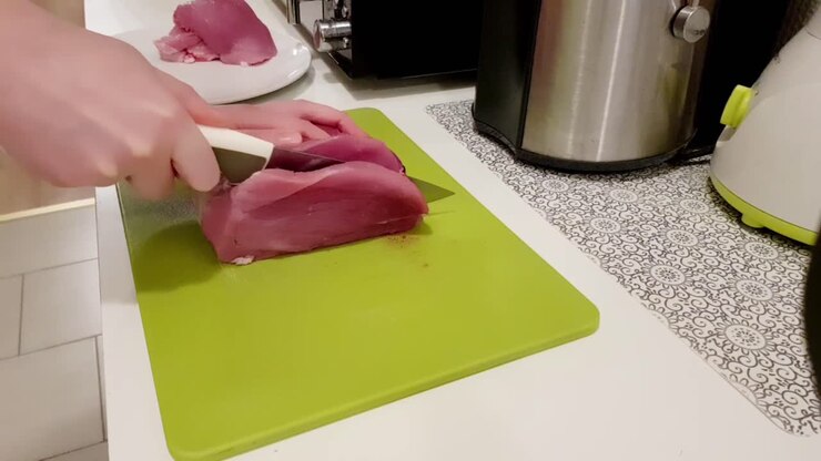 Donna caucasica che taglia carne di maiale con un coltello bianco su un tagliere verde